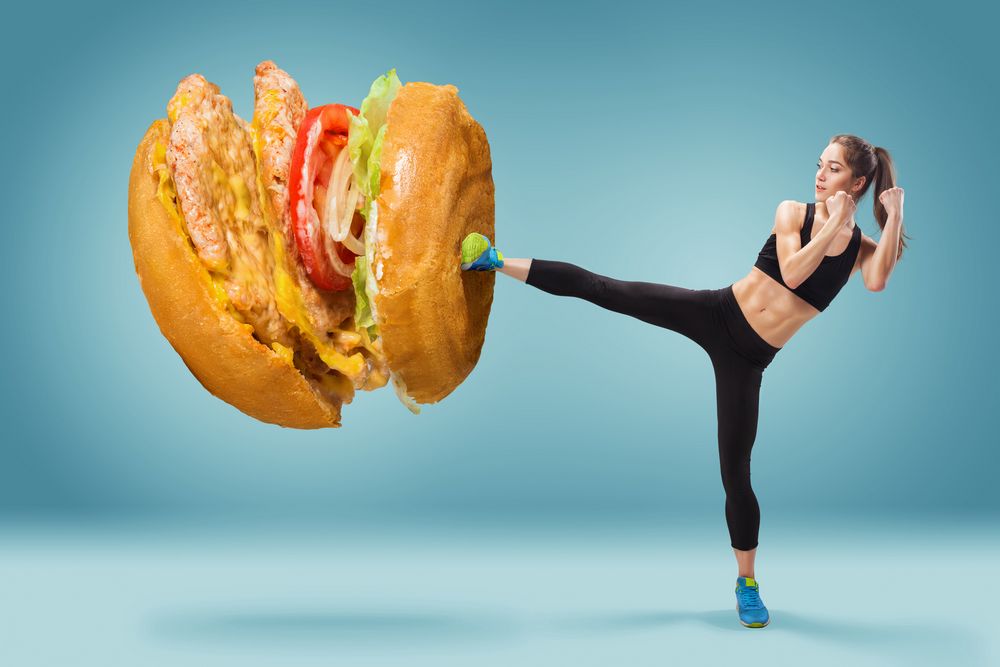 Fit, young, energetic woman boxing hamburger as unhealthy food